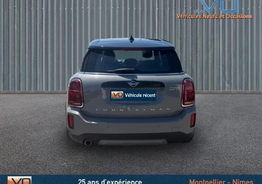 Vue arrière d'une MINI Countryman gris clair avec feux rouges et toit noir sur fond urbain neutre.