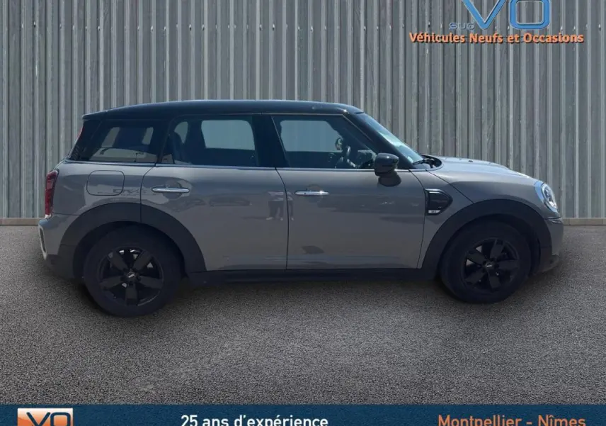 Profil côté gauche d'une MINI Countryman gris clair avec toit noir et jantes alliage noires sur fond industriel.