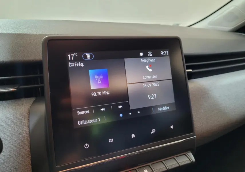 Écran tactile central de la Renault Clio gris foncé affichant radio et téléphone, vue intérieure côté passager.