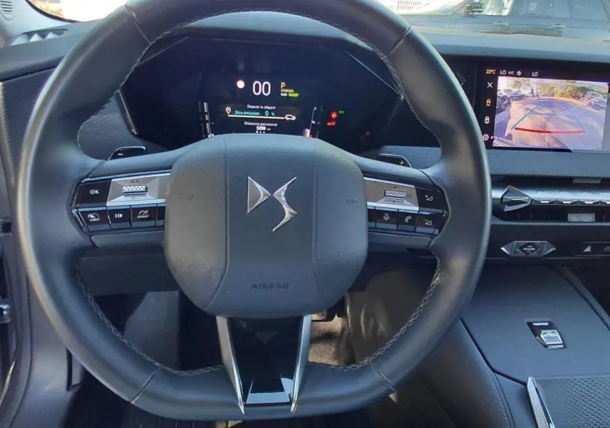Vue intérieure centrée sur le volant noir du DS4 Hybride 2024, avec tableau de bord numérique et écran tactile affichant la caméra de recul.