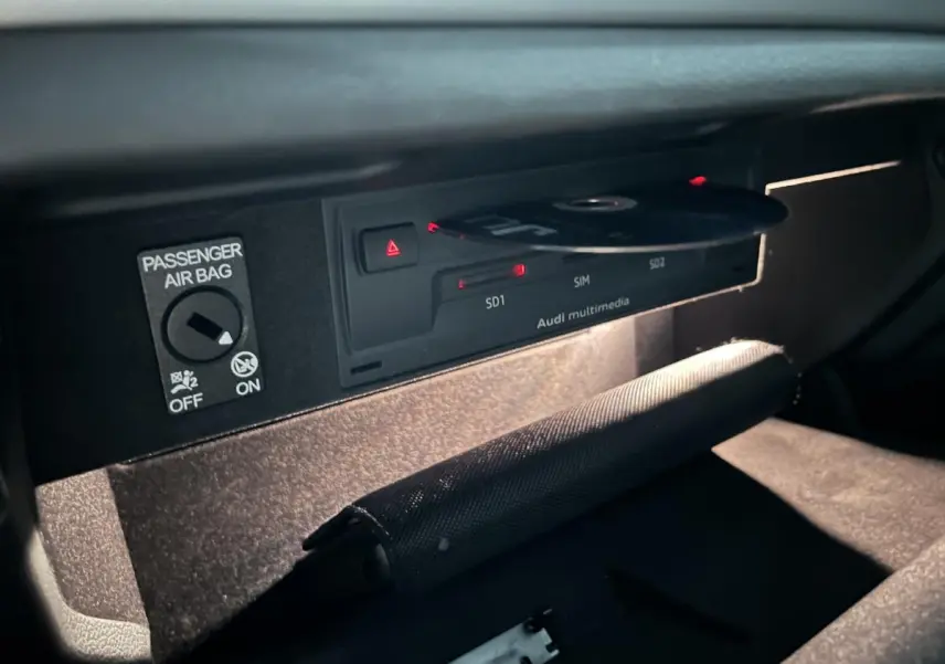 Gros plan sur la boîte à gants ouverte de l'Audi A3 noire, montrant le lecteur Audi multimedia avec un CD inséré.