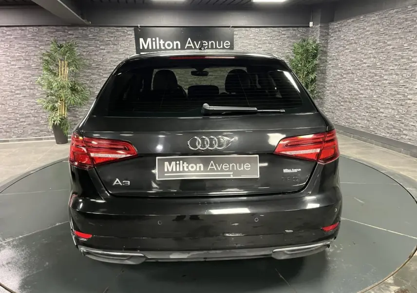 Vue arrière d'une Audi A3 noire avec logo et plaques Milton Avenue dans un showroom intérieur.