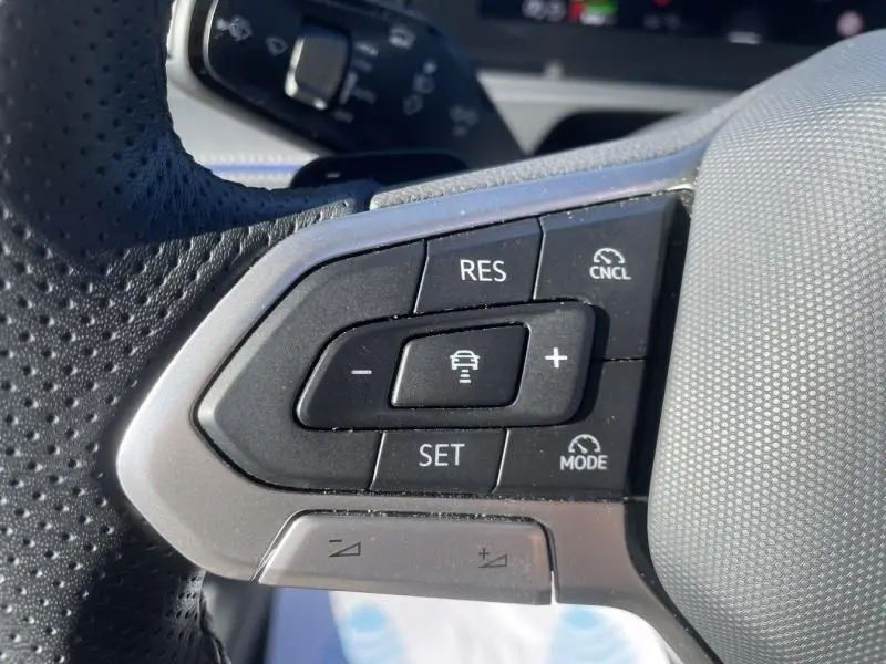 Gros plan sur les commandes au volant côté gauche du Volkswagen Tiguan 1.5 eHybrid gris métal, boutons de régulateur adaptatif visibles.