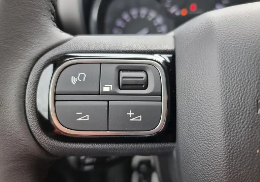 Gros plan sur les commandes de volume et téléphone au volant du Citroën C3 Aircross, intérieur noir.