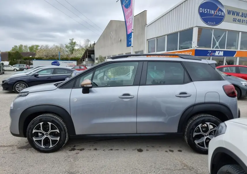 Profil côté gauche d'une Citroën C3 Aircross gris Artence avec jantes alliage diamantées et barres de toit noires.