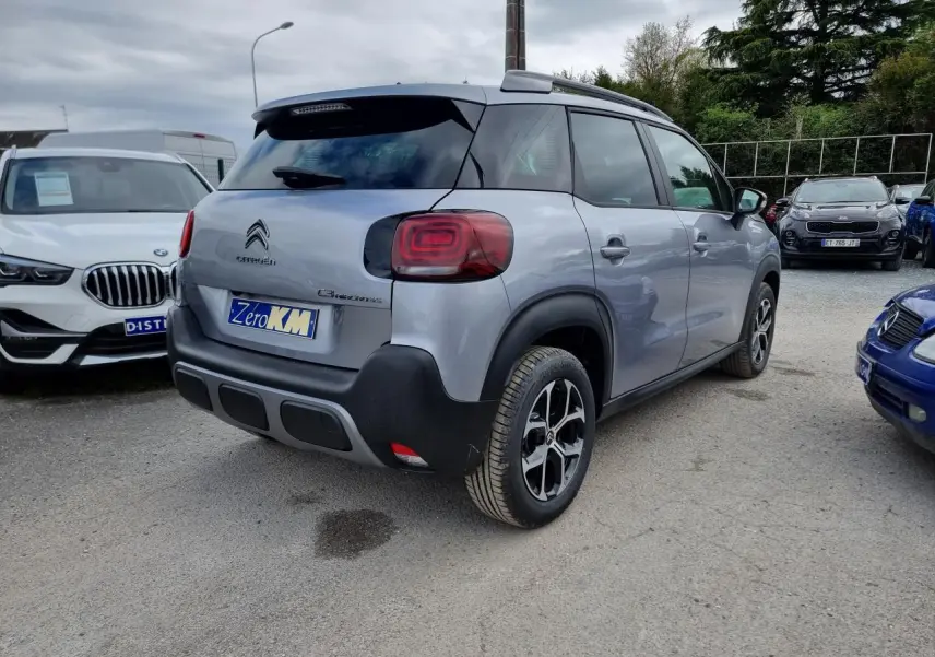Vue 3/4 arrière droite d'un Citroën C3 Aircross gris Artence avec jantes alliage et barres de toit noir brillant.