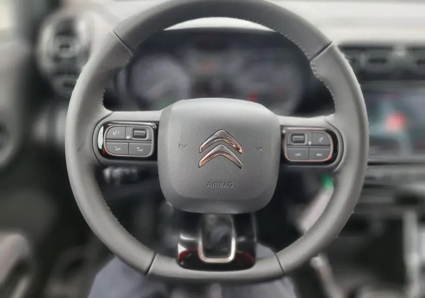 Vue rapprochée du volant noir du Citroën C3 Aircross 2022 avec commandes intégrées et logo chromé central.