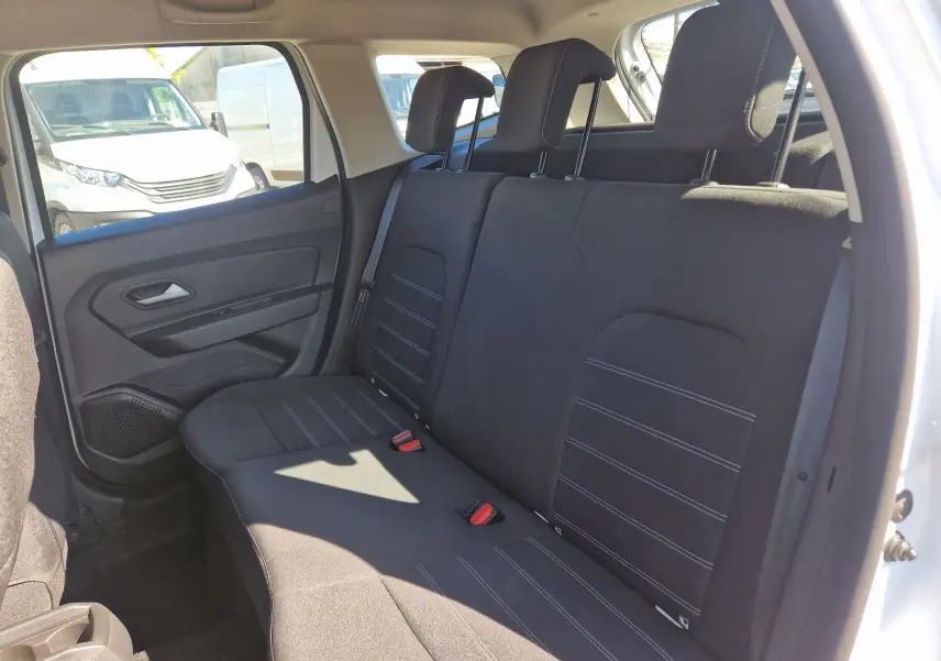 Vue intérieure côté droit montrant la banquette arrière noire du Dacia Duster 4x4 blanc, avec appuie-têtes et ceintures visibles.