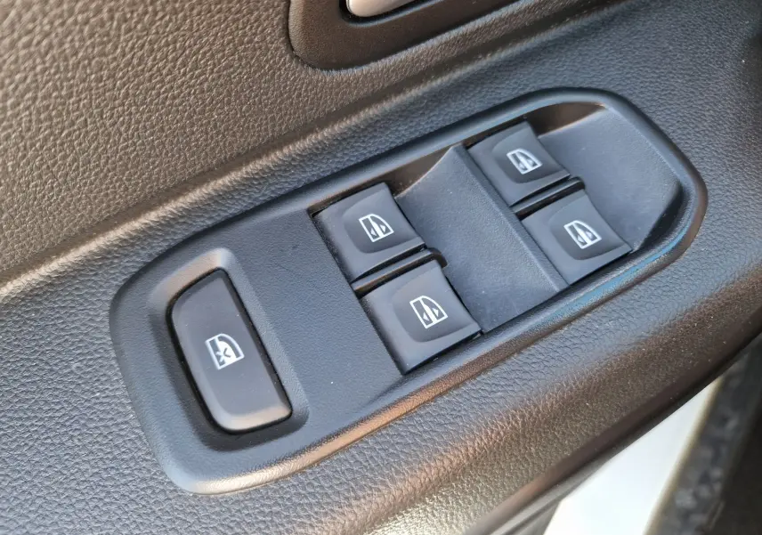 Gros plan sur les commandes électriques des vitres côté conducteur du Dacia Duster blanc 2024.