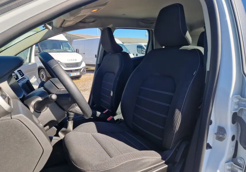 Vue intérieure côté conducteur du Dacia Duster blanc 2024, montrant les sièges avant en tissu noir avec surpiqûres.