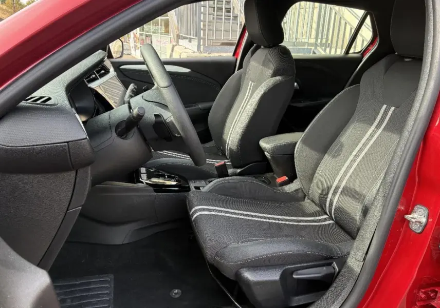 Vue intérieure côté conducteur de l’Opel Corsa 2025 rouge peperoncino, montrant les sièges noirs avec surpiqûres claires.
