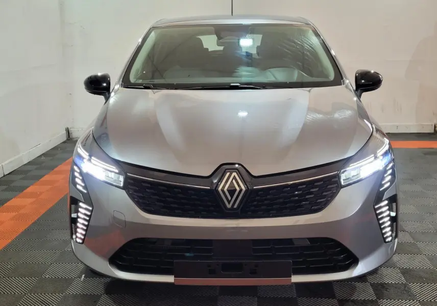 Vue avant d'une Renault Clio gris foncé 2025 avec phares LED allumés et calandre noire distinctive.