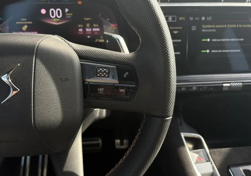 Gros plan sur le volant en cuir perforé noir avec surpiqûres Carmin et Or du DS7 2024, tableau de bord numérique en arrière-plan.