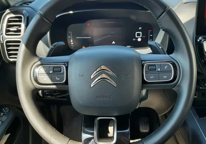 Vue rapprochée du volant noir de la Citroën C5 Aircross Hybrid 136 e-DCS6 Max avec commandes intégrées et tableau de bord numérique.