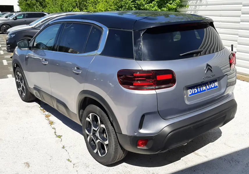 Vue 3/4 arrière droite du Citroën C5 Aircross Hybrid gris acier avec toit noir et jantes bi-ton sur parking extérieur.