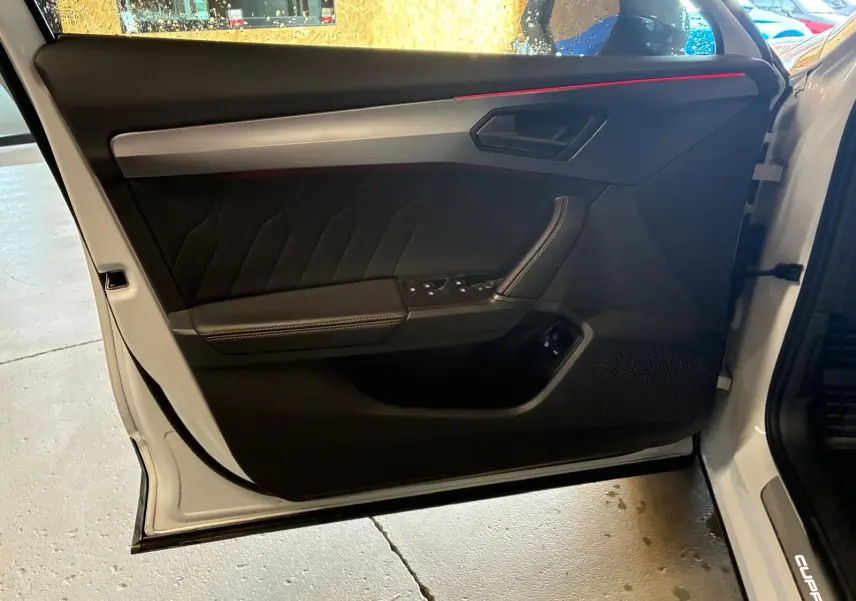 Vue intérieure de la porte avant gauche grise du CUPRA Formentor 1.4 E-HYBRID 2024 avec éclairage d'ambiance rouge.