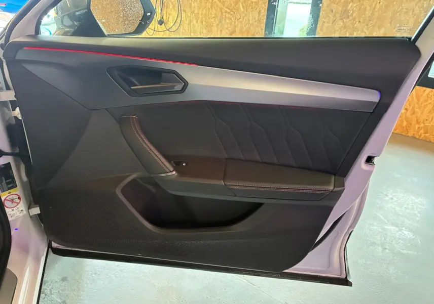 Vue intérieure de la porte avant gauche du CUPRA Formentor gris, avec surpiqûres rouges et bandeau aluminium.