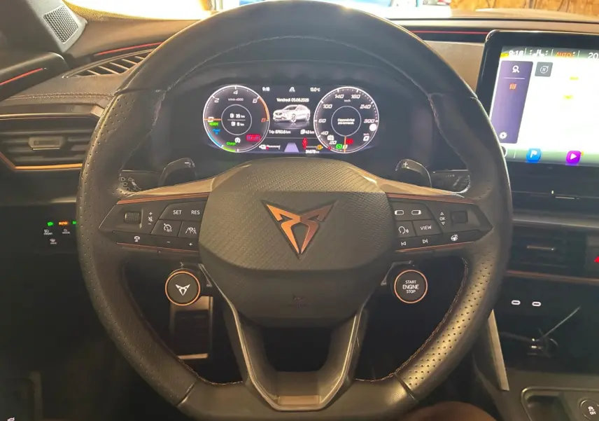 Vue rapprochée du volant noir perforé de la CUPRA Formentor 1.4 E-HYBRID 2024 avec tableau de bord numérique et écran tactile.