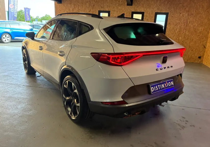 Vue 3/4 arrière droite d'une CUPRA Formentor gris métallisé avec feux arrière allumés dans un garage.