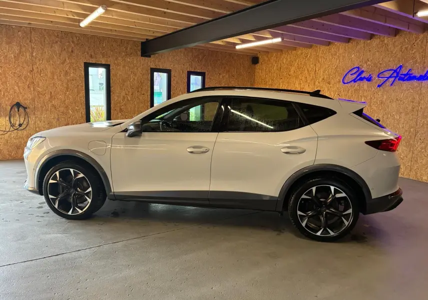 Vue de profil côté gauche du CUPRA Formentor gris clair 2024 en hybride rechargeable, avec jantes noires et toit noir dans un garage.