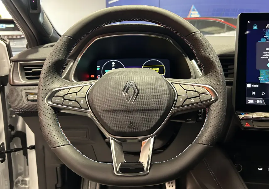 Vue rapprochée du volant chauffant noir perforé du Renault Captur II Ph.2 blanc nacré, avec commandes intégrées.