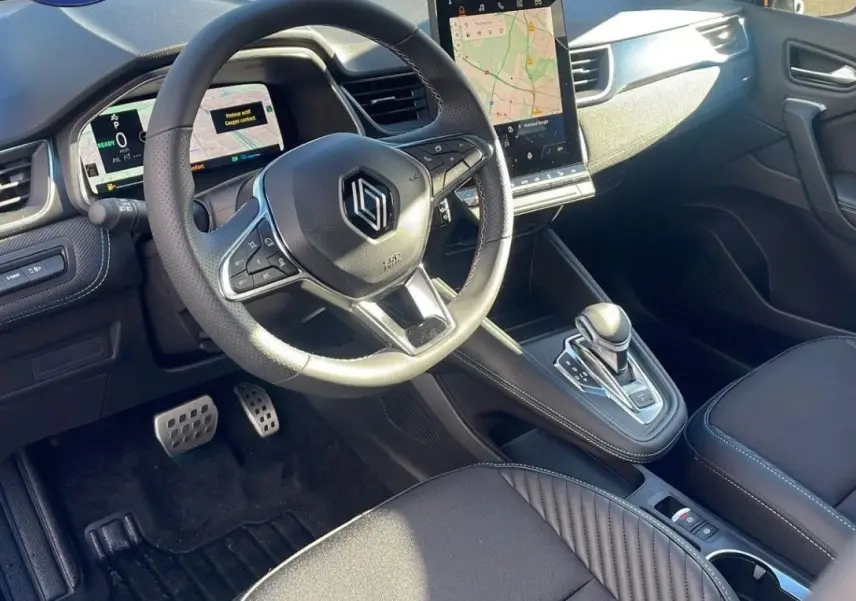 Vue intérieure côté conducteur du Renault Captur blanc nacré, volant chauffant et écran tactile central visible.