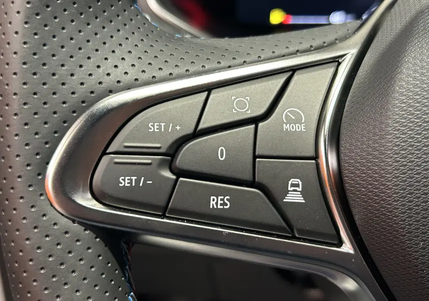 Gros plan sur les commandes noires du volant chauffant perforé du Renault Captur blanc nacré, version hybride 2026.