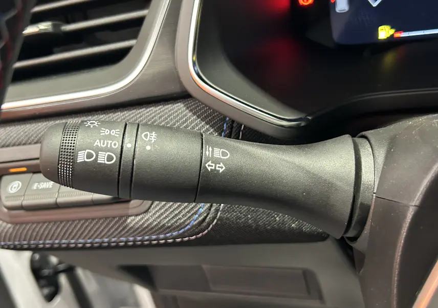 Gros plan sur la commande des feux et clignotants du Renault Captur blanc nacré, intérieur avec surpiqûres bleues.
