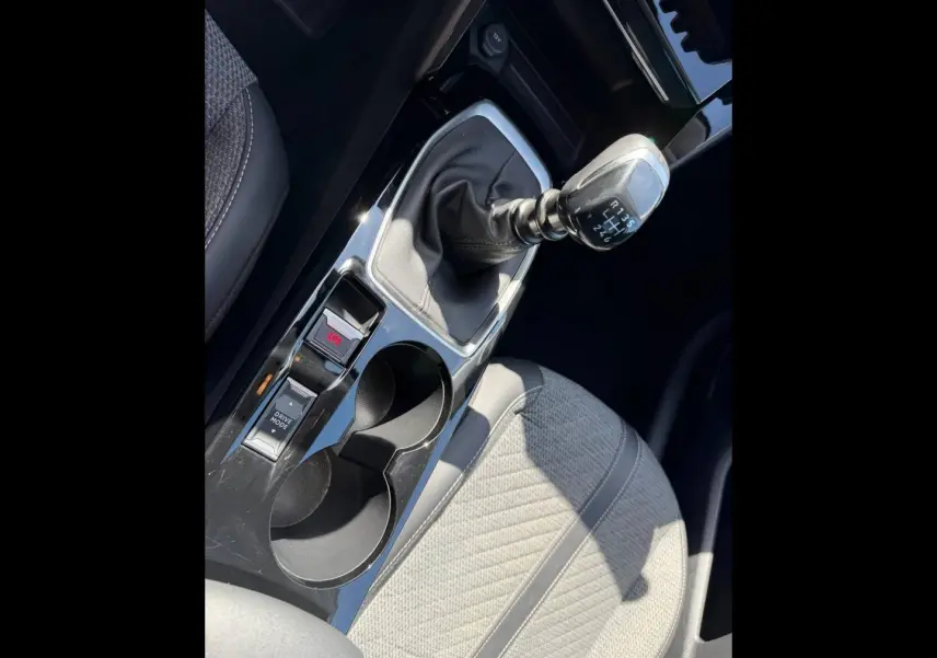 Vue rapprochée de la console centrale de la Peugeot 208 2025 avec levier de vitesse manuel et siège tissu gris clair.