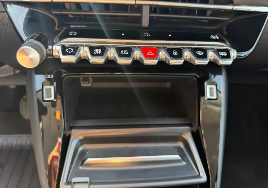 Gros plan sur la console centrale noire brillante de la Peugeot 208 1.2 100ch Allure avec rangements et boutons de commande.
