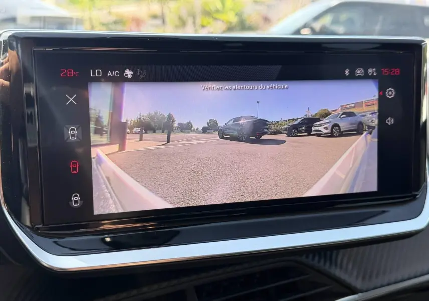 Écran tactile intérieur montrant une caméra de recul avec vue arrière sur un parking ensoleillé.