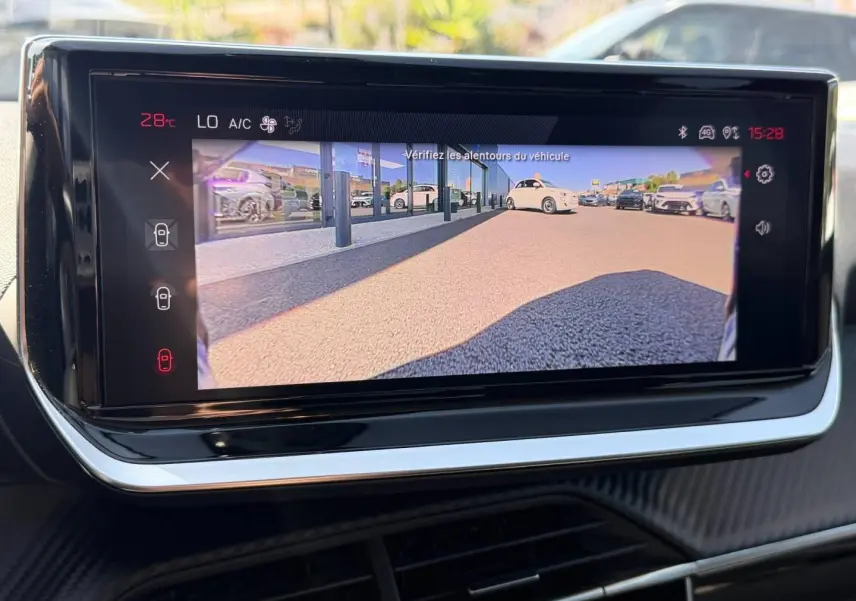 Écran tactile central de la Peugeot 208 2025 montrant la caméra de recul avec vue arrière sur un parking extérieur.