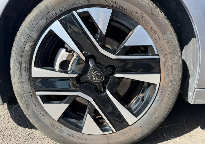 Gros plan sur la jante alu bicolore noire et argentée d'une Peugeot 208 gris Artense, côté avant droit.
