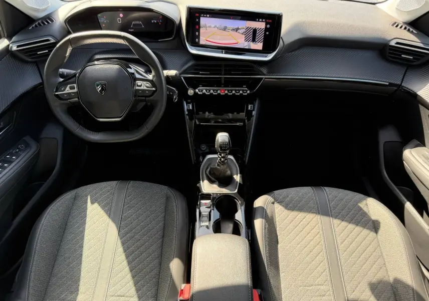 Vue intérieure frontale de la Peugeot 208 1.2 100ch S&S Allure avec tableau de bord noir, écran tactile et sièges tissu gris.