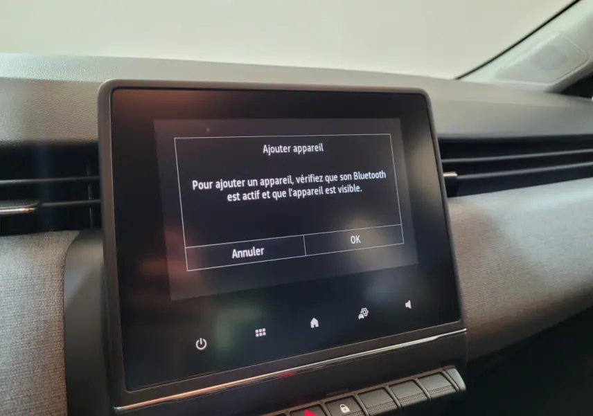 Écran tactile central affichant un message Bluetooth dans l'habitacle clair d'une Renault Clio gris foncé.
