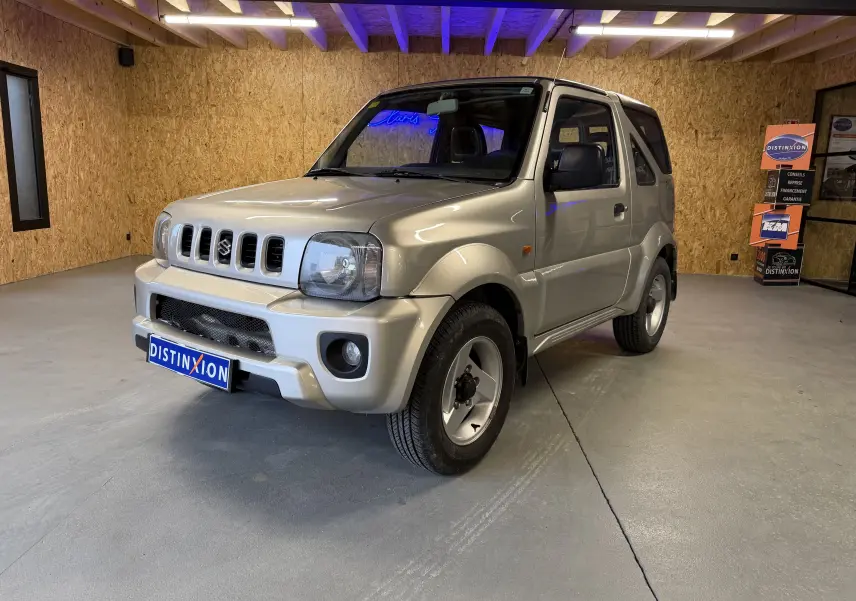 Suzuki Jimny Cabriolet gris en 3/4 avant droit, avec hard-top et jantes alu visibles en intérieur showroom.