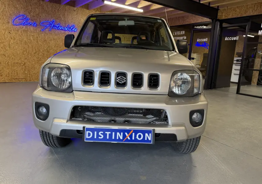 Vue avant d'un Suzuki Jimny Cabriolet gris 2005 avec calandre distinctive et phares carrés, en intérieur showroom.