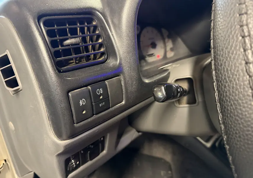 Détail du tableau de bord noir du Suzuki Jimny Cabriolet 2005, avec commandes d’éclairage et ventilation côté gauche du volant.