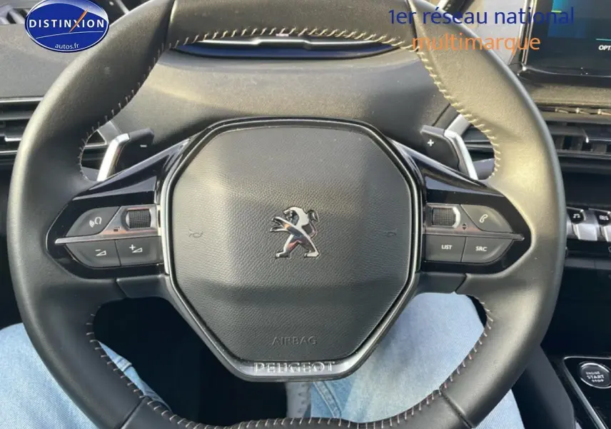 Volant cuir noir multifonction de Peugeot 3008 2024, vue rapprochée centrée sur le logo et commandes au volant.