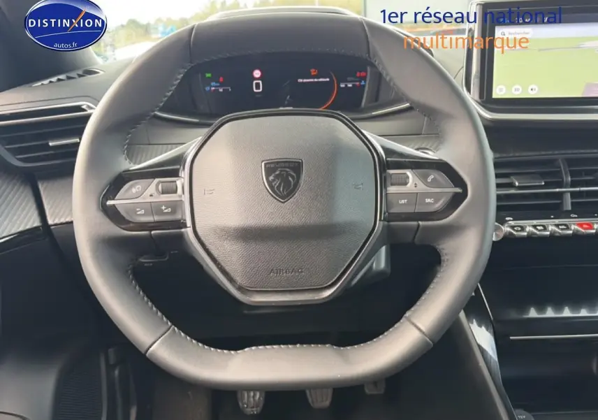 Vue rapprochée du volant noir multifonction de la Peugeot 2008 1.2 100 allure avec tableau de bord digital et écran tactile.