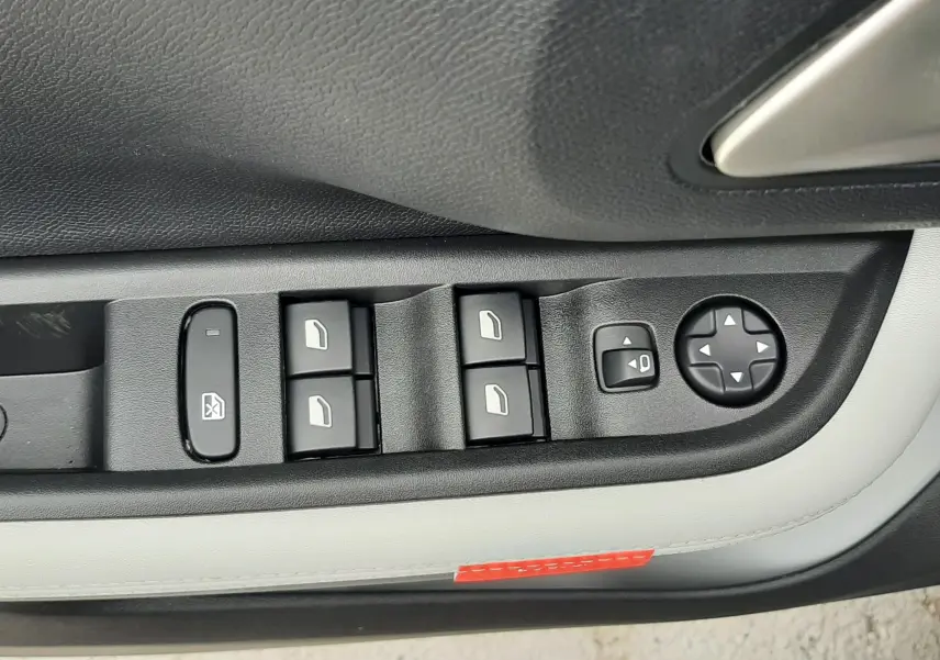Gros plan sur les commandes des vitres et rétroviseurs côté conducteur d'une Citroën C3 Aircross gris Mercury avec intérieur noir et blanc.