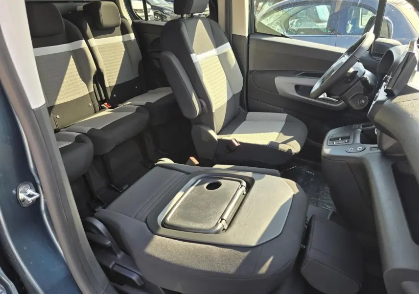 Intérieur du Citroën Berlingo 2025 bleu Kiama, vue côté droit sur sièges tissu gris avec tablette aviation rabattue.