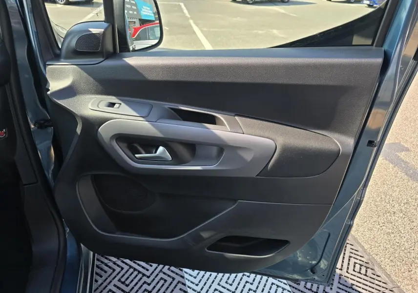 Vue côté gauche de la porte avant ouverte d'un Citroën Berlingo bleu Kiama métal, avec commandes électriques et haut-parleur intégré.