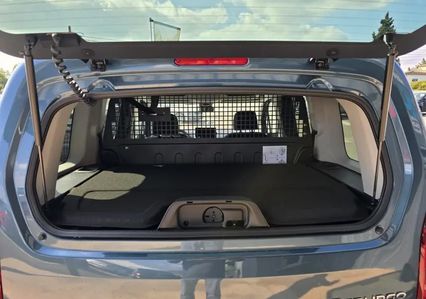 Vue arrière du coffre ouvert d'un Citroën Berlingo bleu Kiama Métal avec séparation grillagée et plancher plat.