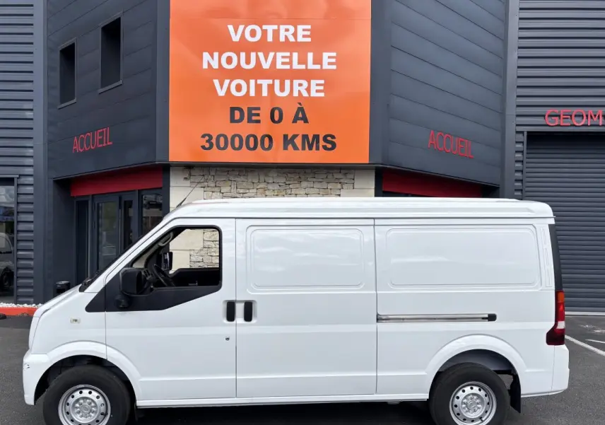 Profil latéral gauche d'un utilitaire blanc DFSK EC35 électrique 2023, sans fenêtres latérales, stationné devant un bâtiment.