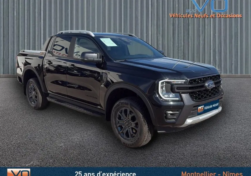 Ford Ranger Wildtrak noir en 3/4 avant droit, avec barres de toit, marchepieds et jantes alliage 18 pouces.