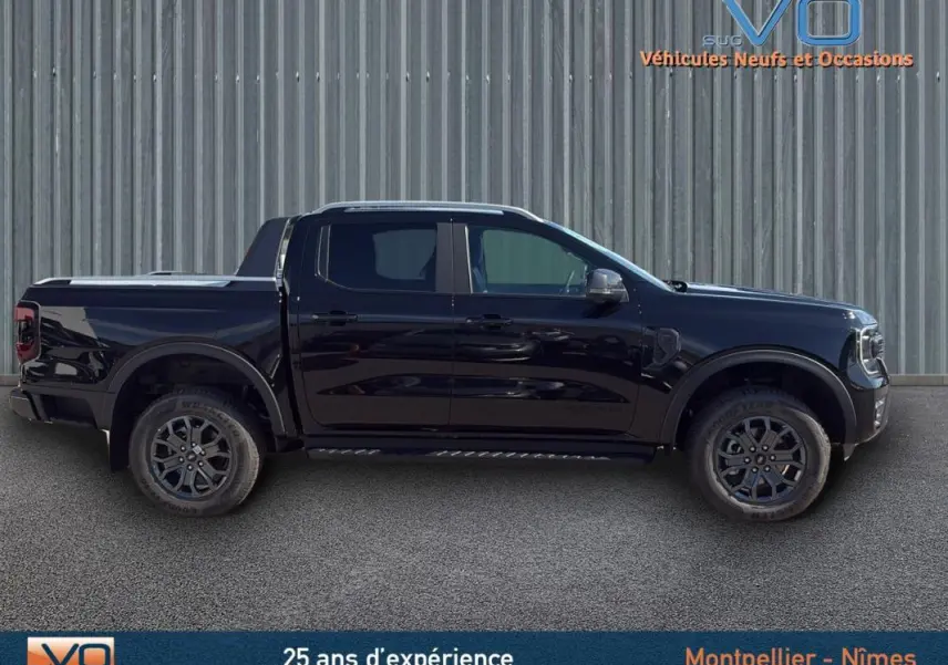 Ford Ranger Wildtrak noir en profil côté gauche, avec barres de toit et marchepieds visibles sur fond industriel.