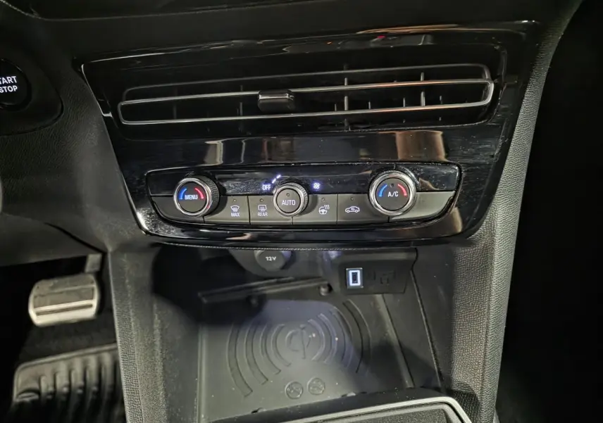Vue rapprochée de la console centrale noire de l’Opel Mokka-e 2025, avec commandes climatisation et recharge smartphone par induction.