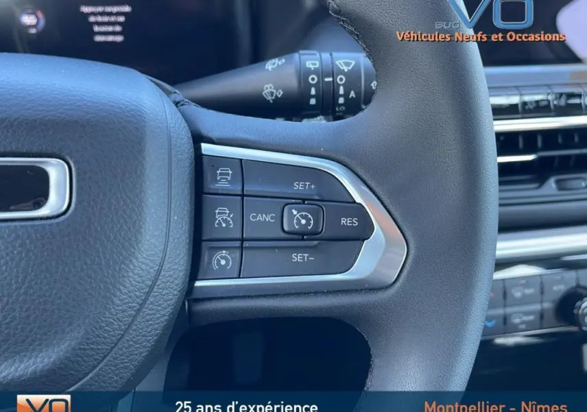 Gros plan sur les commandes du régulateur de vitesse au volant d'un Jeep Compass blanc 2024, intérieur moderne.