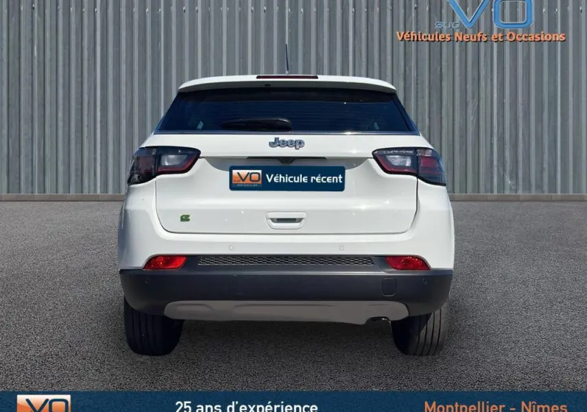 Vue arrière d'un Jeep Compass blanc 2024 avec feux arrière sombres et logo Jeep visible sur fond urbain.